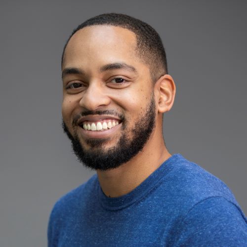 A photo of Martez wearing a blue shirt in front of a grey background.